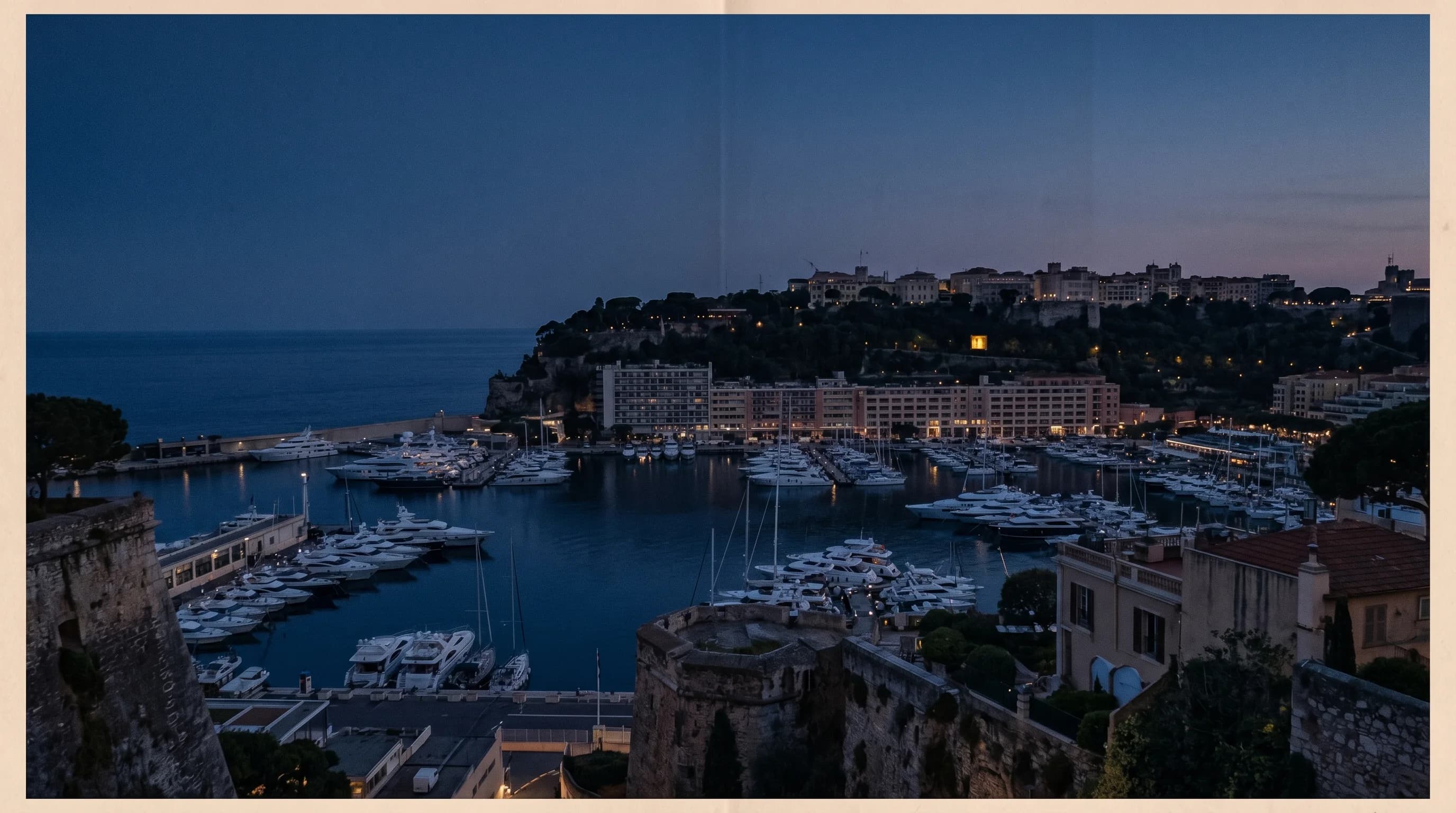 Photographie aérienne éditoriale de la Principauté de Monaco à l'heure bleue, skyline de Monte-Carlo et port avec yachts.